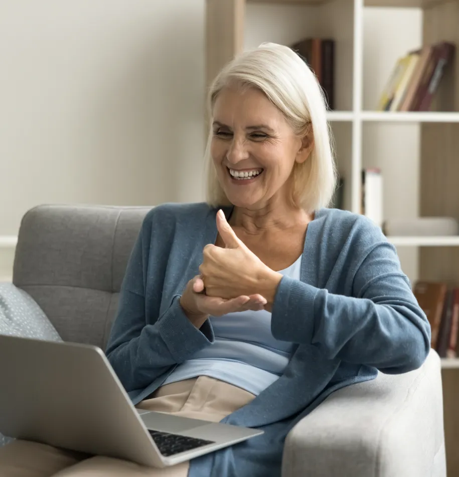 A woman sits on her couch using a silver laptop.